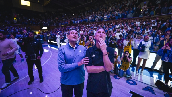 Two coaches on the court looking up at screen during college basketball game