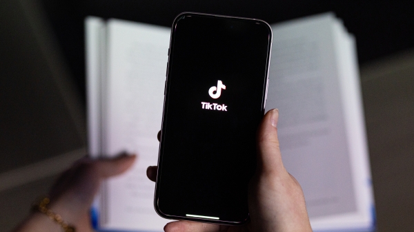 Photo of a hand holding a phone with the Tik Tok logo in front of a book.