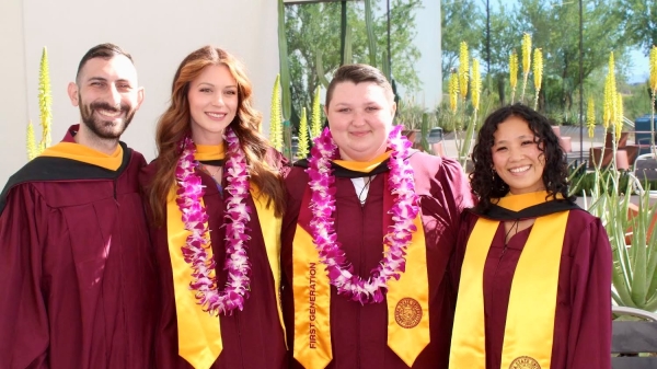 Four people in graduation gowns pose for a photo