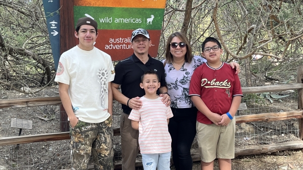 A mom, dad and three kids pose for a photo in front of a zoo sign