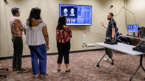 Students listen to a professor speak in front of a screen displaying motion capture technology.