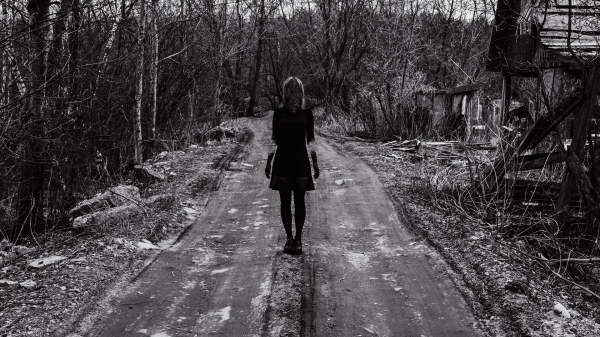 Black-and-white photo of a girl with no face in the middle of a tree-lined road.