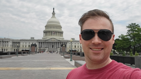 A man with sunglasses stands in front of the U.S. Capitol building on an overcast day.