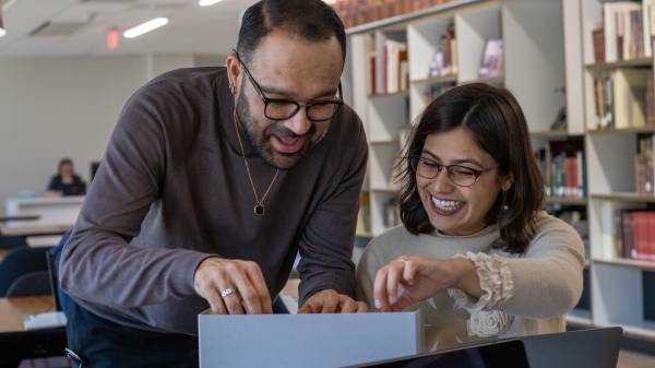 Faculty and fellow Mellissa Linton and Francisco Carrillo smiling while searching through physical files. 