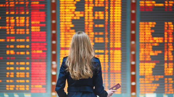 Woman seen from behind looking at a flight board an an airport.