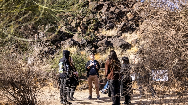 A guide leading a group of people on a tour of a outdoor petroglyph preserve