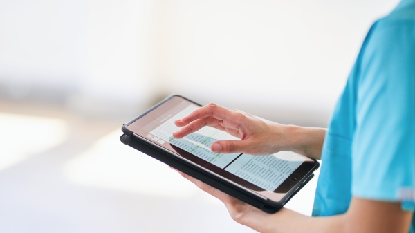 Health professional in blue scrubs holding electronic pad