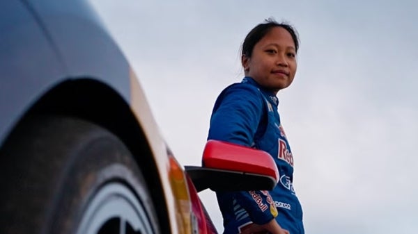 Woman in racing suit leaning on sports car