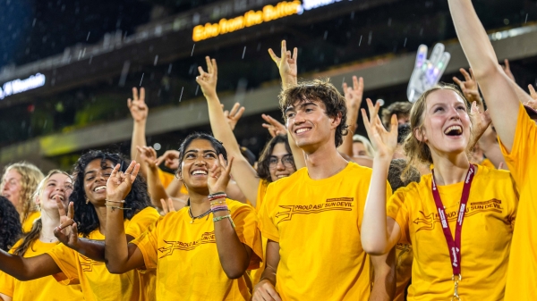 Group of students wearing gold t-shirts making pitchfork students in football stadium in the rain