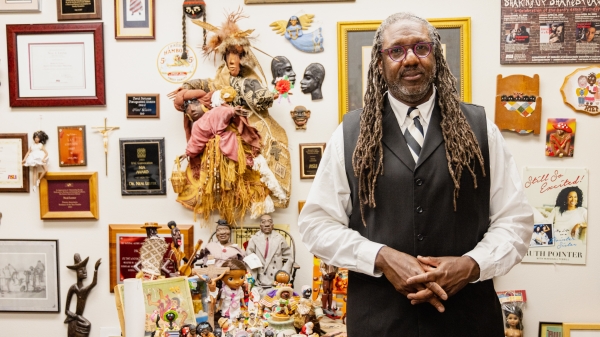 Neal Lester standing in front of a wall with awards, figurines, dolls, posters and other objects. 