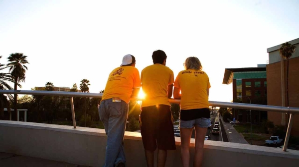 3 ASU students on a bridge look over University Drive as the sun sets