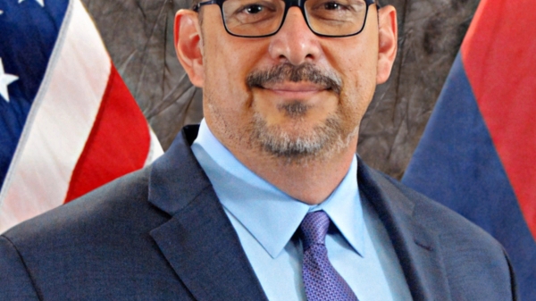 Portrait of Adrian Fontes looking at the camera with U.S. flags in the background.