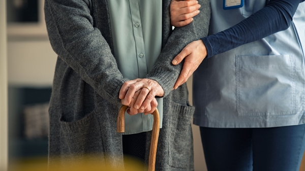 Close-up of a nurse's hands on the arm of an older person with cane.