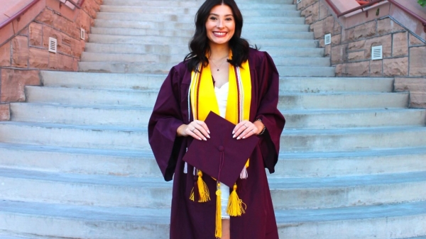 ASU grad Alia Rocha standing on a staircase while wearing graduation regalia.