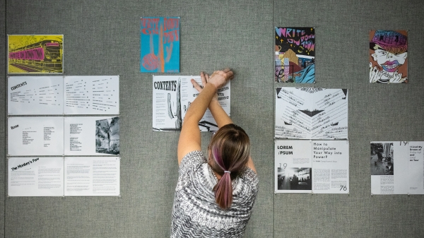 shot of a woman from the back, pinning an illustration to a wall with many illustrations already pinned on it