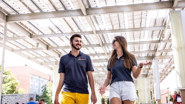 Two young people talking as they walk down a path below a solar panel shade structure.