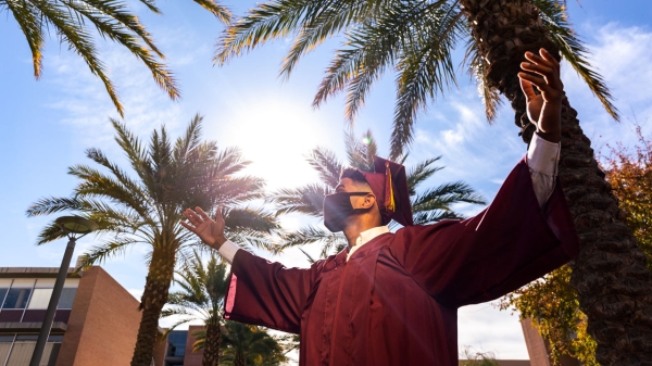 Graduate in commencement cap and gown looks up, arms out - ready to take on the world.