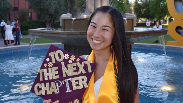 ASU grad Joyce Yen at the Old Main fountain with a graduation cap decorated to say "to the next chapter"