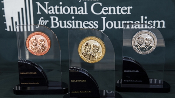 Awards made of glass and metal on a table in front of a sign that reads "Donald W. Reynolds National Cente for Business Journalism."