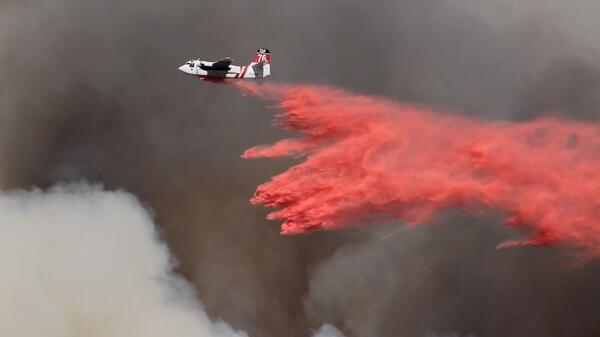 Plane flies through dark clouds dispersing a red substance.