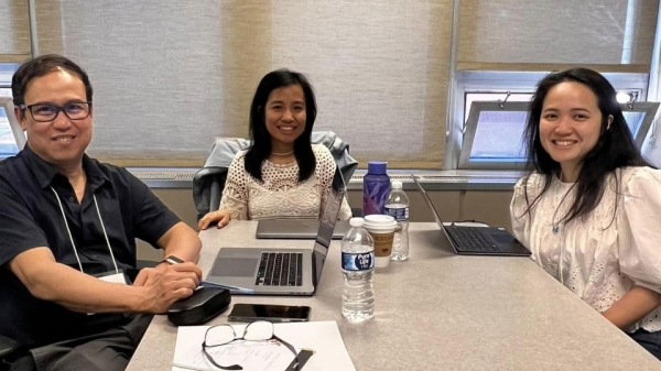 Three people sit at a conference table while looking toward the camera and smiling.