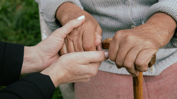 A woman holds on to the hand of an older person who is holding a cane.