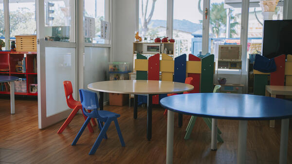 Empty children's tables and chairs in a room with windows.