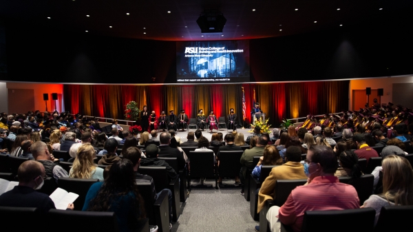 People seated in an auditorium with graduates on the right side in their caps and gowns.