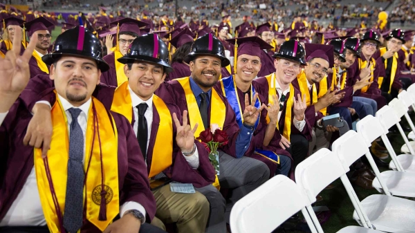 Del E. Webb School of Construction graduates seated in a row wearing graduation attire and hard hats.