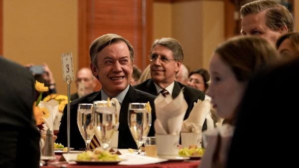 ASU President Michael Crow smiles as he sits at a banquet table surrounded by others