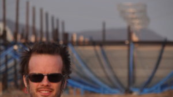 ASU Assistant Professor Daniel Jacobs wearing sunglasses and standing in front of the HERA radio telescope site in South Africa.