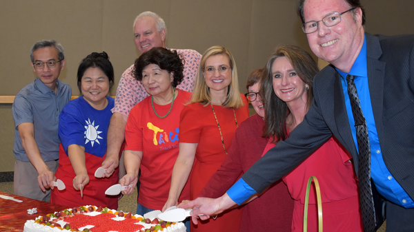 People smile and pose for a group photo while holding knives to a cake.