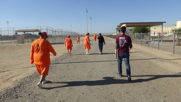 People in orange jumpsuits walk on an outdoor track.