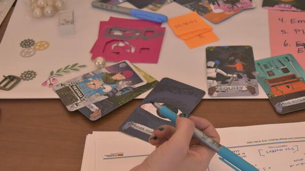 Cards from the Humane Tech Card Deck spread over a desk with various craft materials and notes