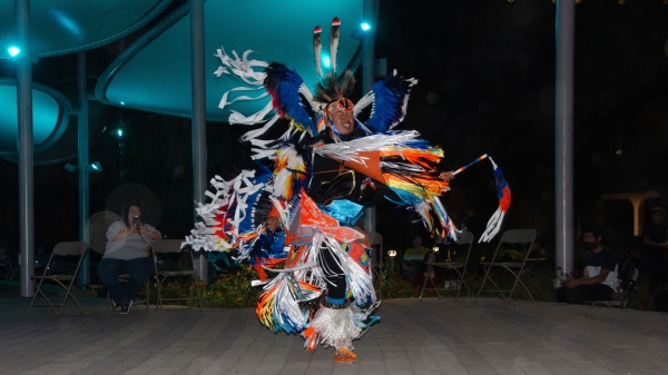 A Native American dancer in full regalia performs on an outdoor stage