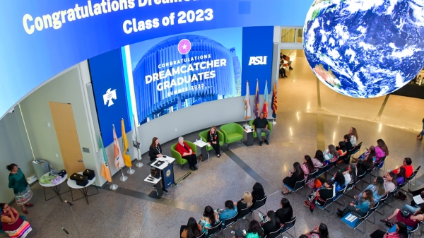 A group of people gathered in a room, sitting in chairs, with a digital sign above that says "Congratulations DreamCatcher Graduates Class of 2023"