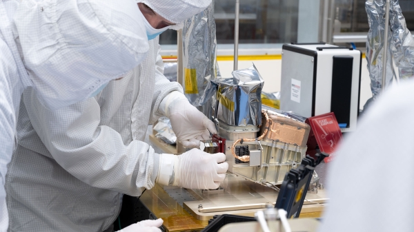 People in full body suits work on a piece of space equipment