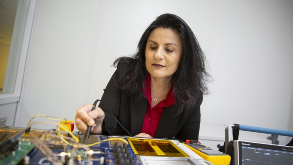 Woman seated at a table working with microelectronics.