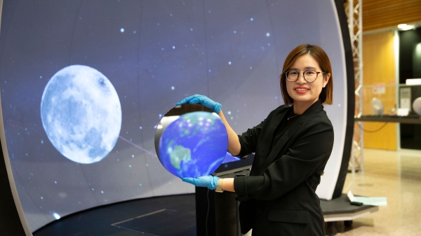 Ying-Chen "Daphne" Chen stands in front of a screen displaying the moon while holding semiconductor material reflecting a model of the Earth