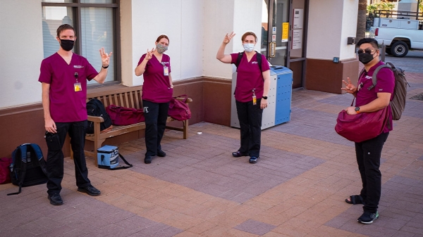 Four nursing students in scrubs and face makss pose for a photo throwing pitch forks