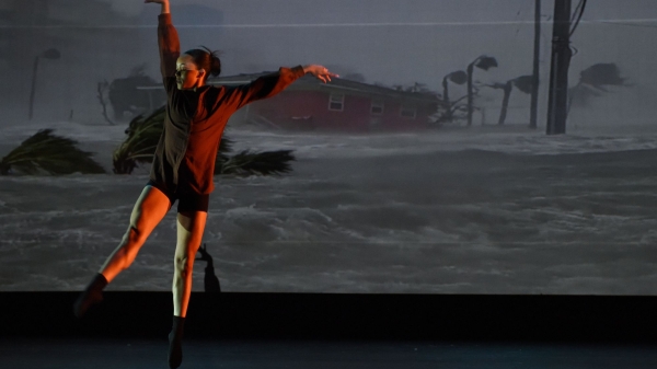 A dancer performs in front of a screen depicting a hurricane