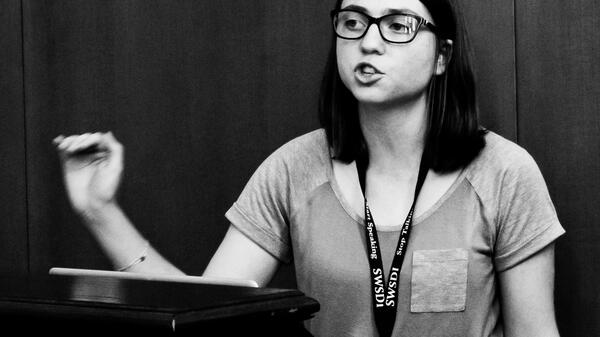 female high school student standing behind a lecturn delivering a speech