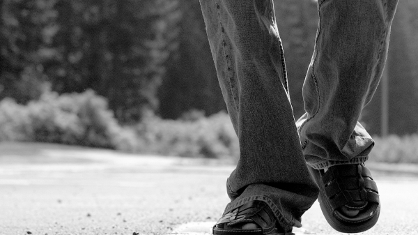 A closeup of someone&#039;s feet walking down a road.