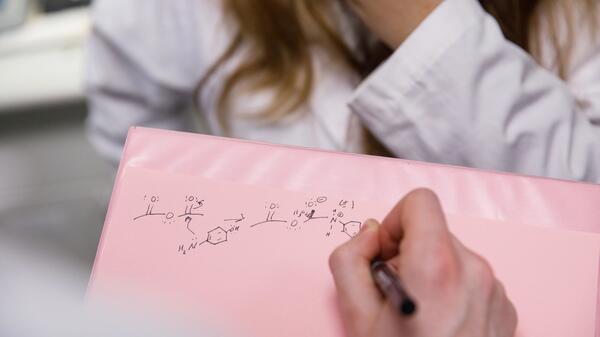 Hand writing a chemistry equation on a piece of paper.