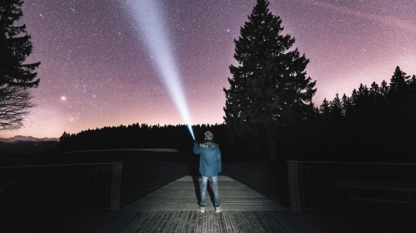 photo of man shining flashlight at starry sky