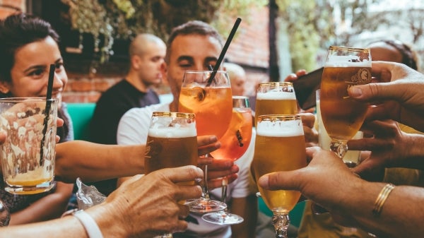 People seated around a table holding acloholic beverages clinking them together in a "cheers" motion.