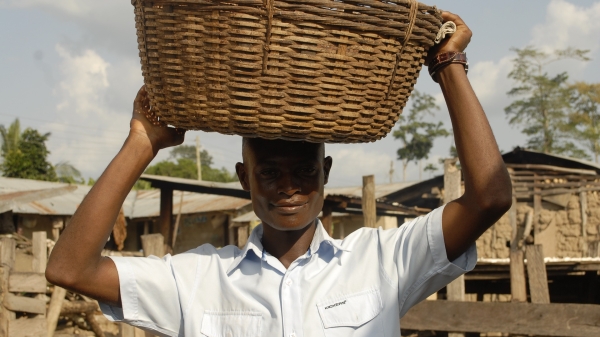 Man in an outdoor setting holding a woven basket on his head.