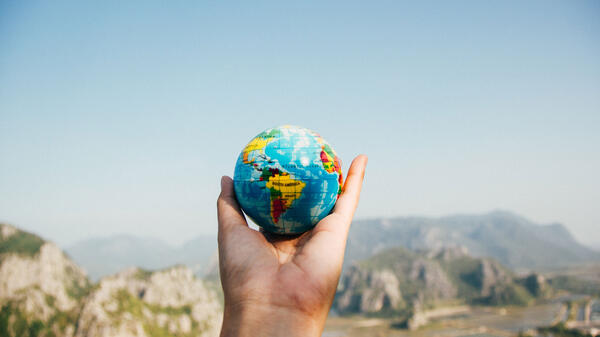 Hand holding a small globe in front of mountains in the distance.