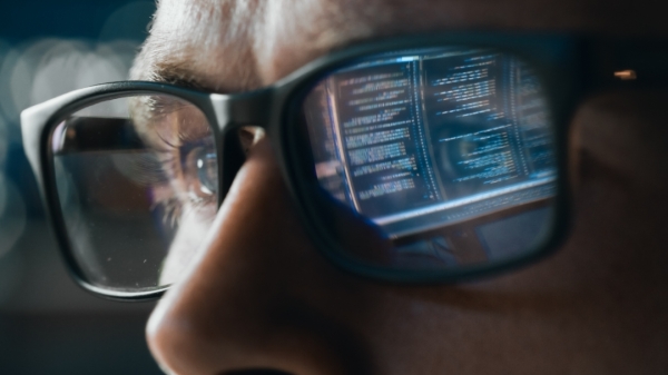 Close-up of a face wearing glasses that reflect a computer screen.