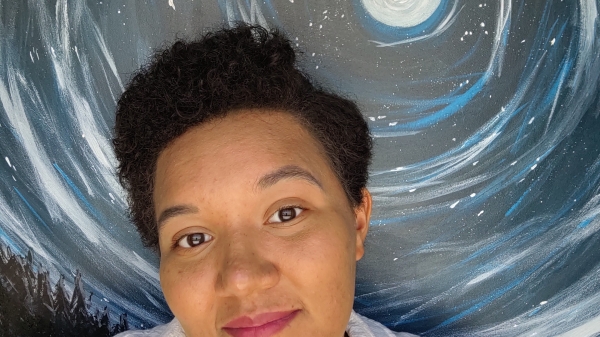 Hanan Robinson poses in front of artwork depicting an interstellar scene.